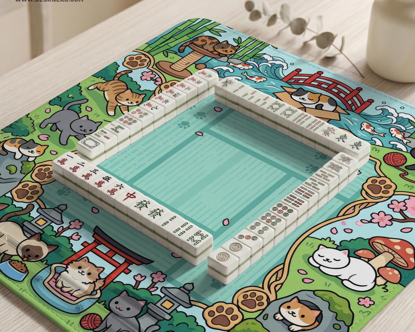 Mint green mahjong mat with a cat garden border, koi fish, bamboo, blossoms, and scenic details around an open center.