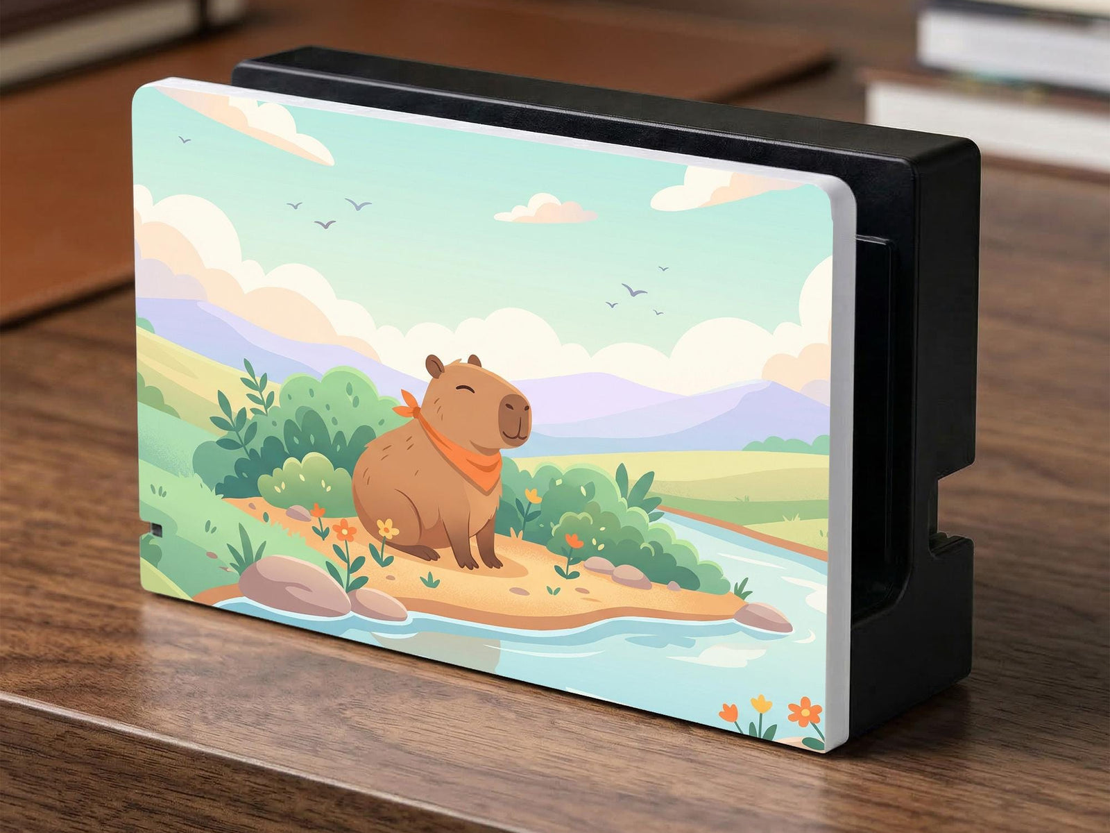 A pastel Switch case with a smiling capybara, green hills, a river, and a soft muted sky.