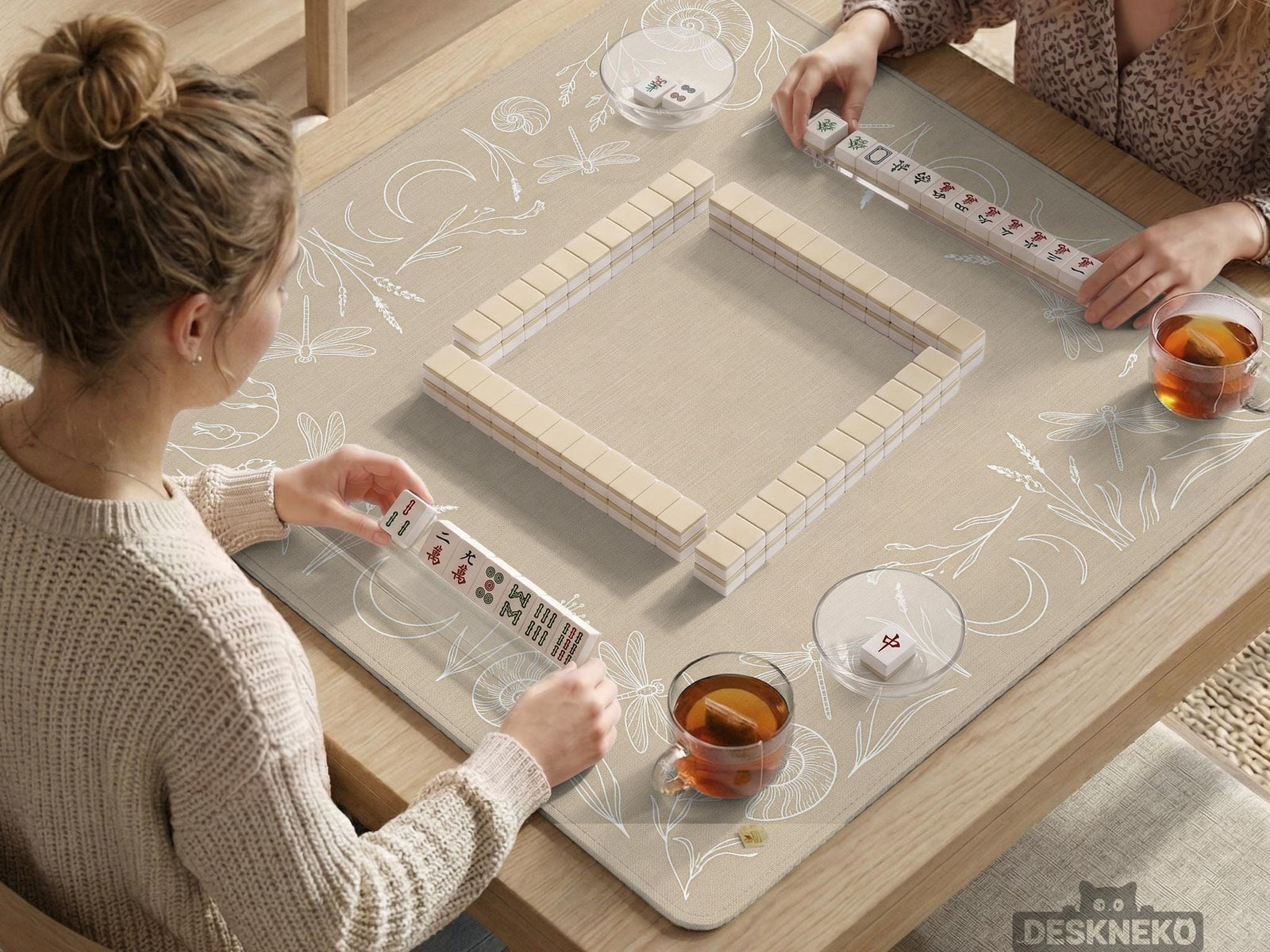 A square beige mahjong mat with a thin illustrated border of dragonflies, crescent moons, grasses, and shell motifs around a blank center.