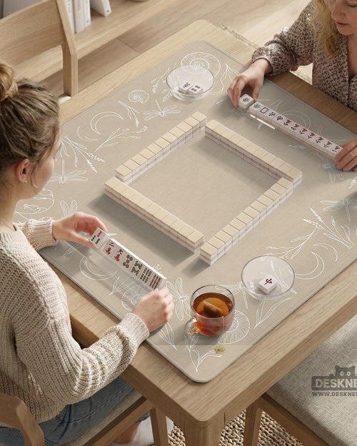 A square beige mahjong mat with a thin illustrated border of dragonflies, crescent moons, grasses, and shell motifs around a blank center.