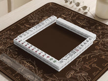 Dark brown mahjong table mat with a botanical border of moths, mushrooms, keys, vines, and small celestial details around a plain open center.