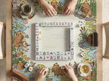 A square mahjong mat with a capybara illustration, pastel spring garden border, sakura blossoms, ducks, bamboo, streams, and a blank center play area.