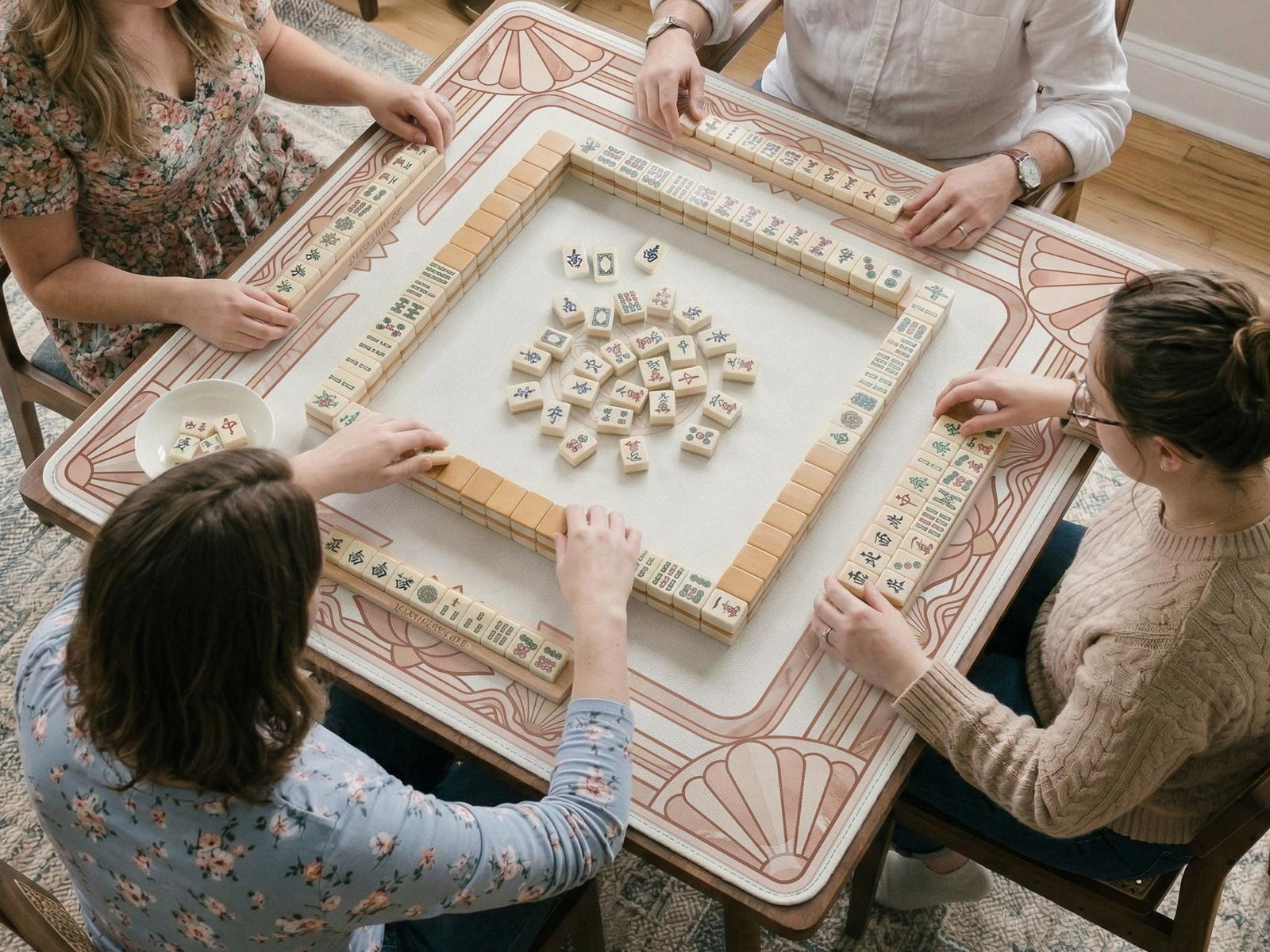 Square blush pink mahjong mat with an art deco border, lotus motifs, and shell details on a light background.