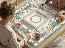 Sage green square mahjong mat with bamboo stalks and cherry blossom branches printed across the surface.