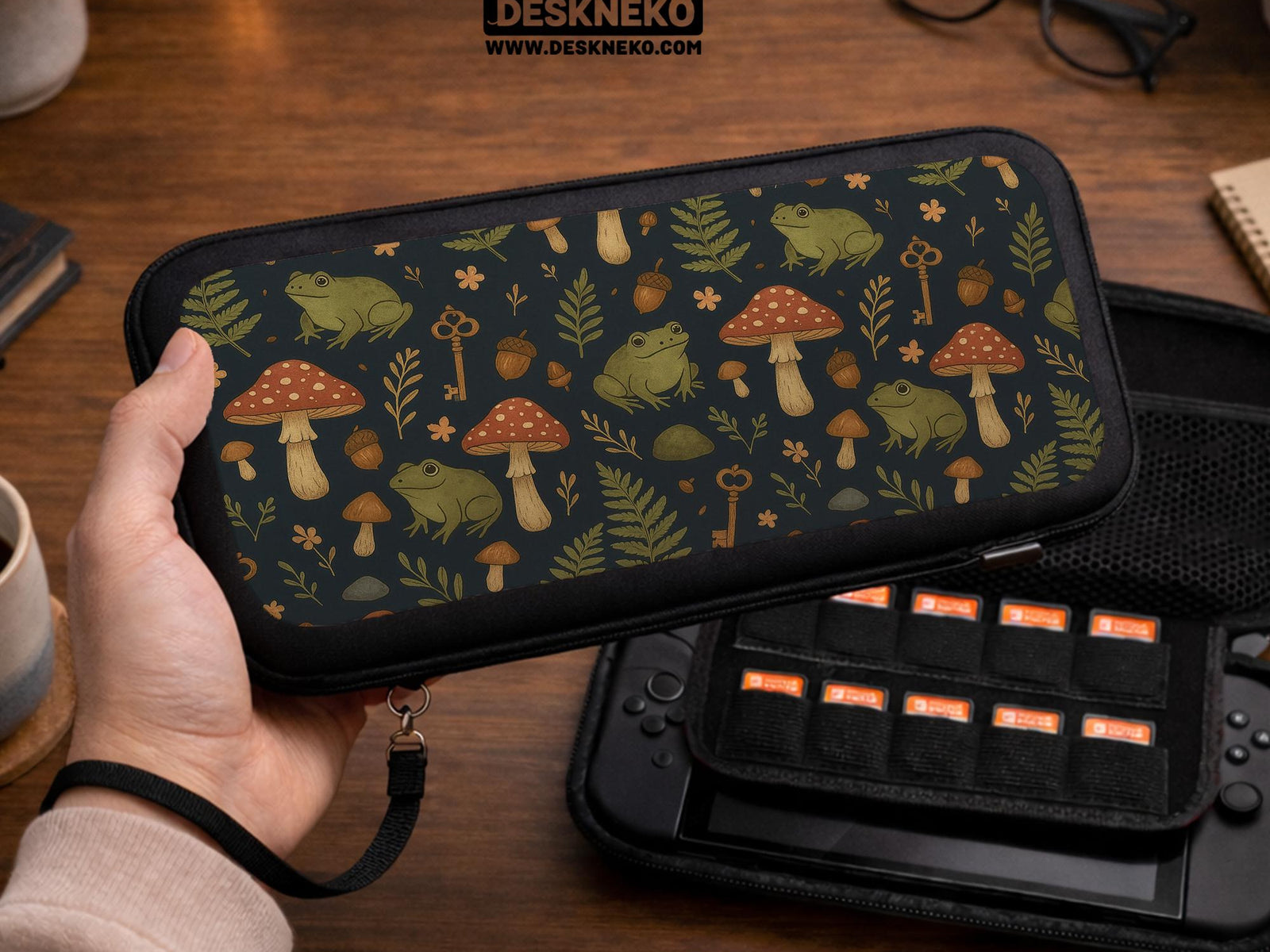 A navy Switch case printed with green frogs, red mushrooms, ferns, acorns, and small vintage keys in a woodland pattern.
