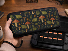 A navy Switch case printed with green frogs, red mushrooms, ferns, acorns, and small vintage keys in a woodland pattern.