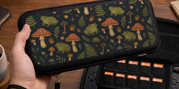 A navy Switch case printed with green frogs, red mushrooms, ferns, acorns, and small vintage keys in a woodland pattern.