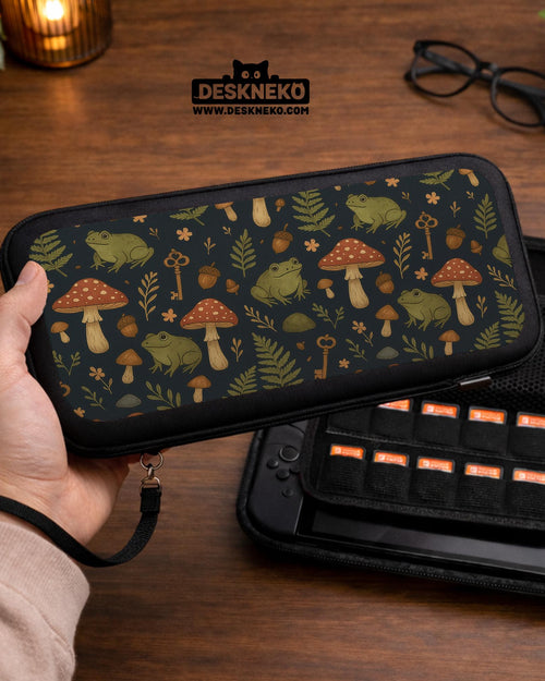 A navy Switch case printed with green frogs, red mushrooms, ferns, acorns, and small vintage keys in a woodland pattern.