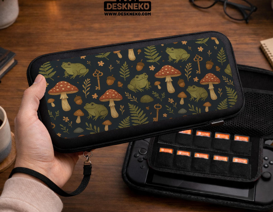 A navy Switch case printed with green frogs, red mushrooms, ferns, acorns, and small vintage keys in a woodland pattern.