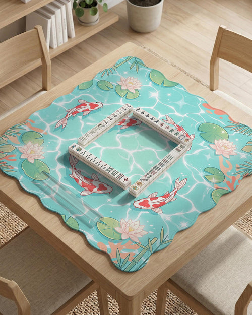 Square mahjong playing mat with aqua background, coral accents, floating lily pads, and koi fish circling the play area.