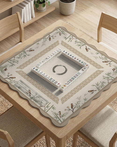 Beige mahjong mat with bamboo accents, small bird illustrations, and a clear center area.
