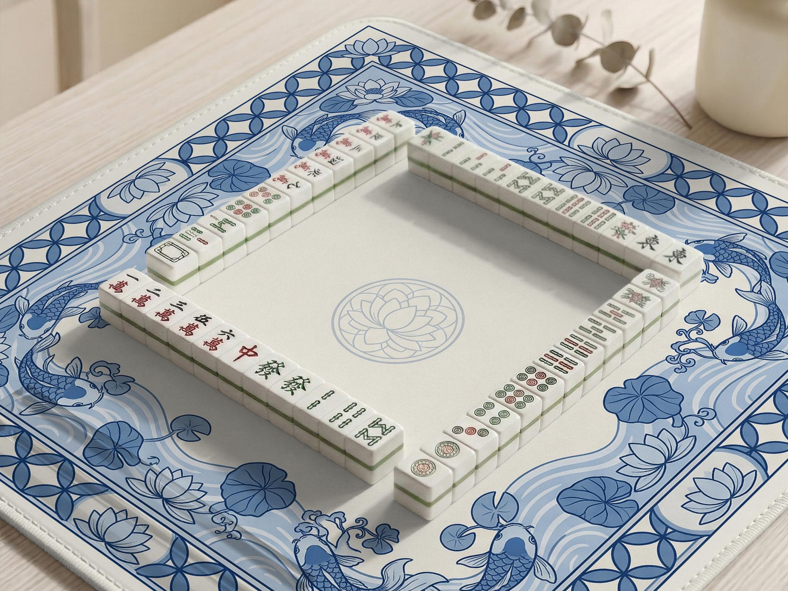 Blue and white square mahjong table mat with koi fish, lotus flowers, water lilies, and flowing wave patterns around a plain center.