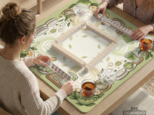 Sage green mahjong table mat with illustrated teacups, leaves, latte art circles, and floral corner details around an open center.