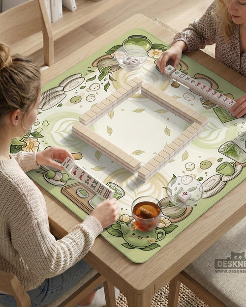 Sage green mahjong table mat with illustrated teacups, leaves, latte art circles, and floral corner details around an open center.
