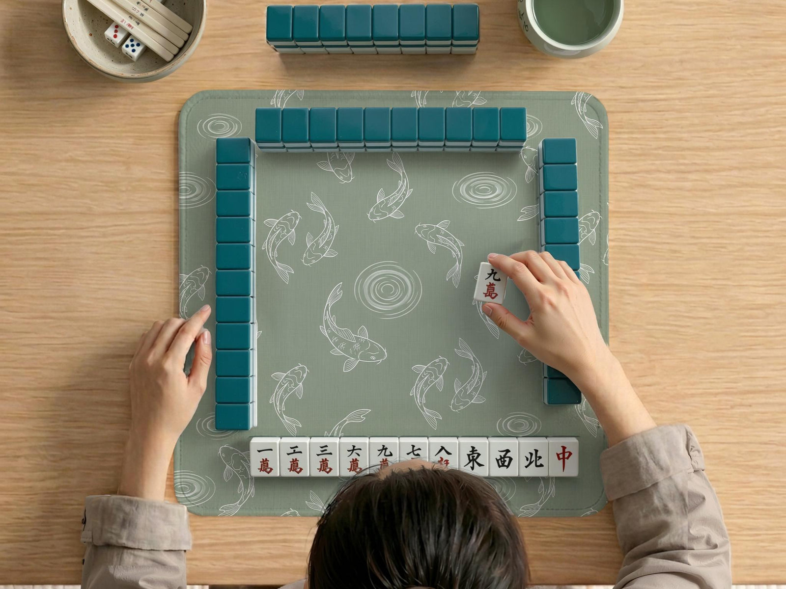 Sage green square mahjong mat with white koi fish line art and water ripple pattern.