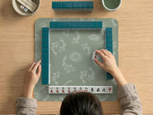 Sage green square mahjong mat with white koi fish line art and water ripple pattern.