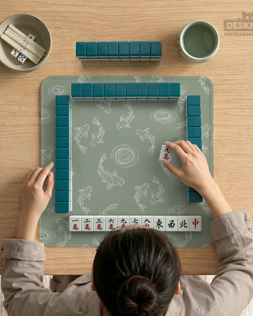 Sage green square mahjong mat with white koi fish line art and water ripple pattern.