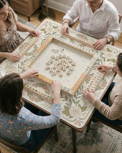 Square mahjong mat with a light floral border in sage green, cream, and blush around a plain center play area.