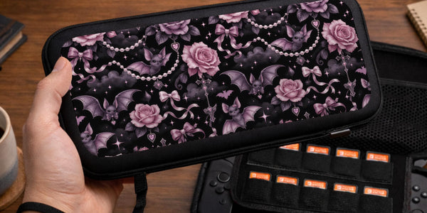 A black Switch carrying case with a pink gothic rose print, small bats, ribbon bows, pearl chain details, and tiny sparkles.