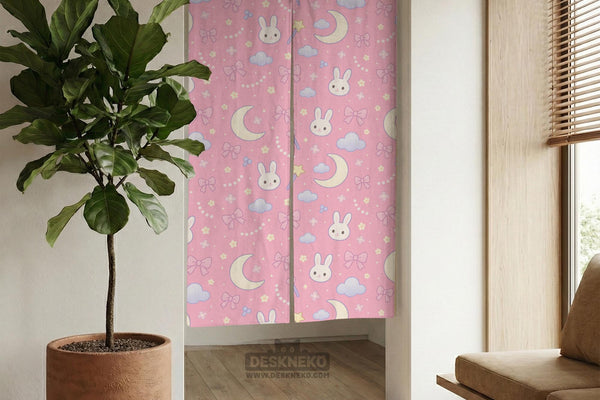 Pink noren curtain with cute bunny faces, crescent moons, blue clouds, bows, stars, and small flowers on a warm pink background.