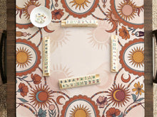 A square terracotta mahjong mat with suns, crescent moons, and floral accents around a patterned border and open center.