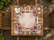 A square mahjong mat with a scalloped edge, sun and moon artwork, terracotta flowers, a soft cream background, and a decorative border around the play area.