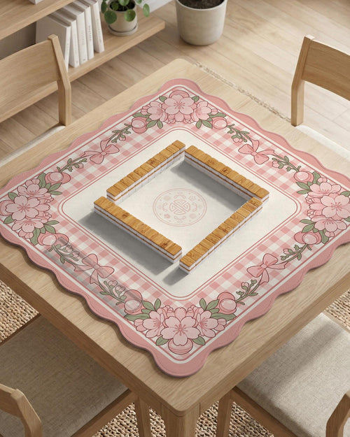 Square pink mahjong mat with a gingham border, floral corner details, and ribbon accents on a light background.