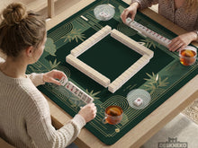 Square emerald green mahjong mat with bamboo line art, gold geometric cloud shapes, and a plain center playing area.