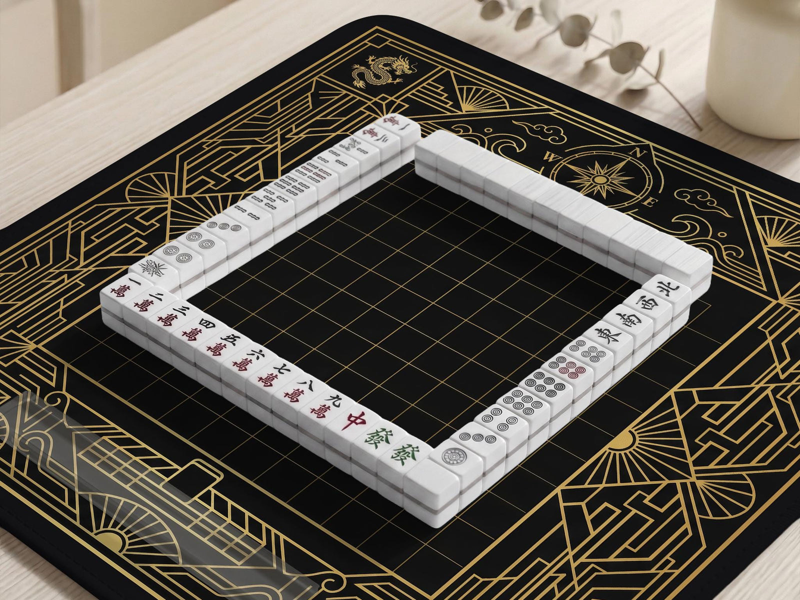 Black mahjong mat with a gold geometric Art Deco border, fan shapes, compass-style details, dragon and phoenix elements, and a plain center play area.
