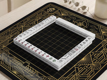 Black mahjong mat with a gold geometric Art Deco border, fan shapes, compass-style details, dragon and phoenix elements, and a plain center play area.