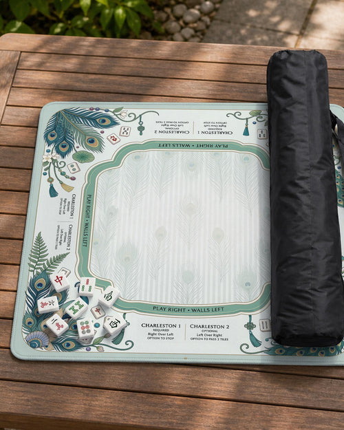 Teal square mahjong mat with peacock feathers, soft floral pattern, tassel details, and printed rule guide text in the center.