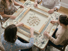 Beige square mahjong mat with a sage border, crane birds, bamboo, blossoms, tile icons, and printed instructions.