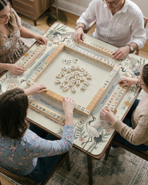 Beige square mahjong mat with a sage border, crane birds, bamboo, blossoms, tile icons, and printed instructions.