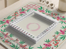 A square mahjong mat with a cream center, pink trellis pattern, green bamboo leaves, and small cherry blossom accents around the edge.