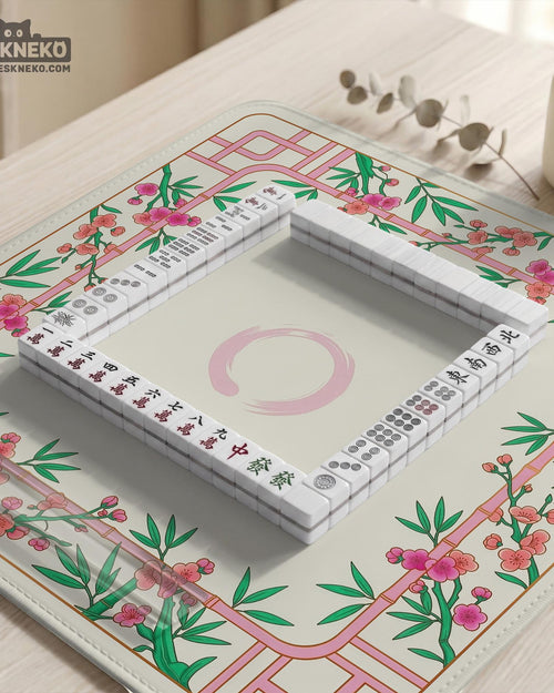 A square mahjong mat with a cream center, pink trellis pattern, green bamboo leaves, and small cherry blossom accents around the edge.