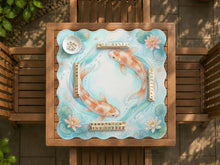 Turquoise square mahjong mat with orange koi fish, cream lotus flowers, lily pads, and soft blue water lines.