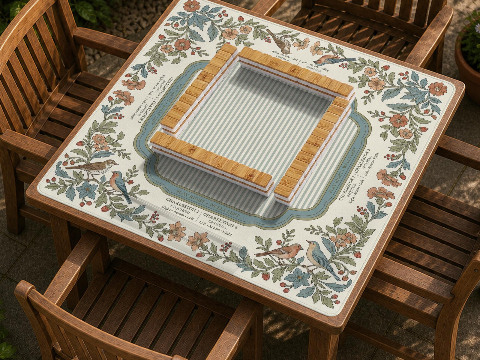 Square mahjong mat with floral botanical artwork around the edges, a light center, soft stripe details, and printed rule bands.