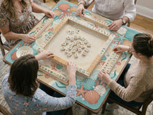Square mahjong mat with a coral and aqua coastal border featuring shells, coral, pearls, starfish, and waves around a clear center.