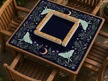 Navy square mahjong mat with a moon, moth, stars, and floral botanical border around an open center play area.