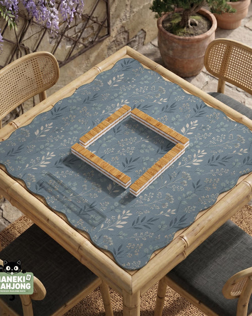 Blue mahjong mat with a botanical floral pattern, pale leaves, and delicate stems on a dusty blue background.