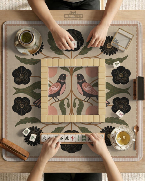 Beige mahjong mat with a folk floral design, a bird, blush pink fruit, olive botanical leaves, black flowers, and a soft woven-look background.
