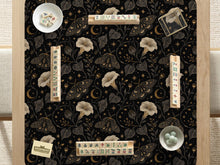 Black square mahjong mat with moths, moonflowers, crescent moons, and scattered stars in a celestial floral pattern.