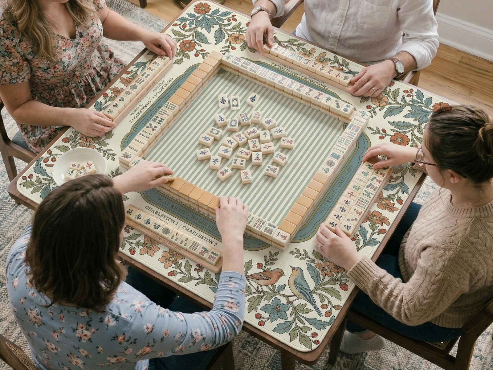 A floral mahjong mat with a cream background, botanical border, soft blue frame, vintage bird garden artwork, and printed rules.