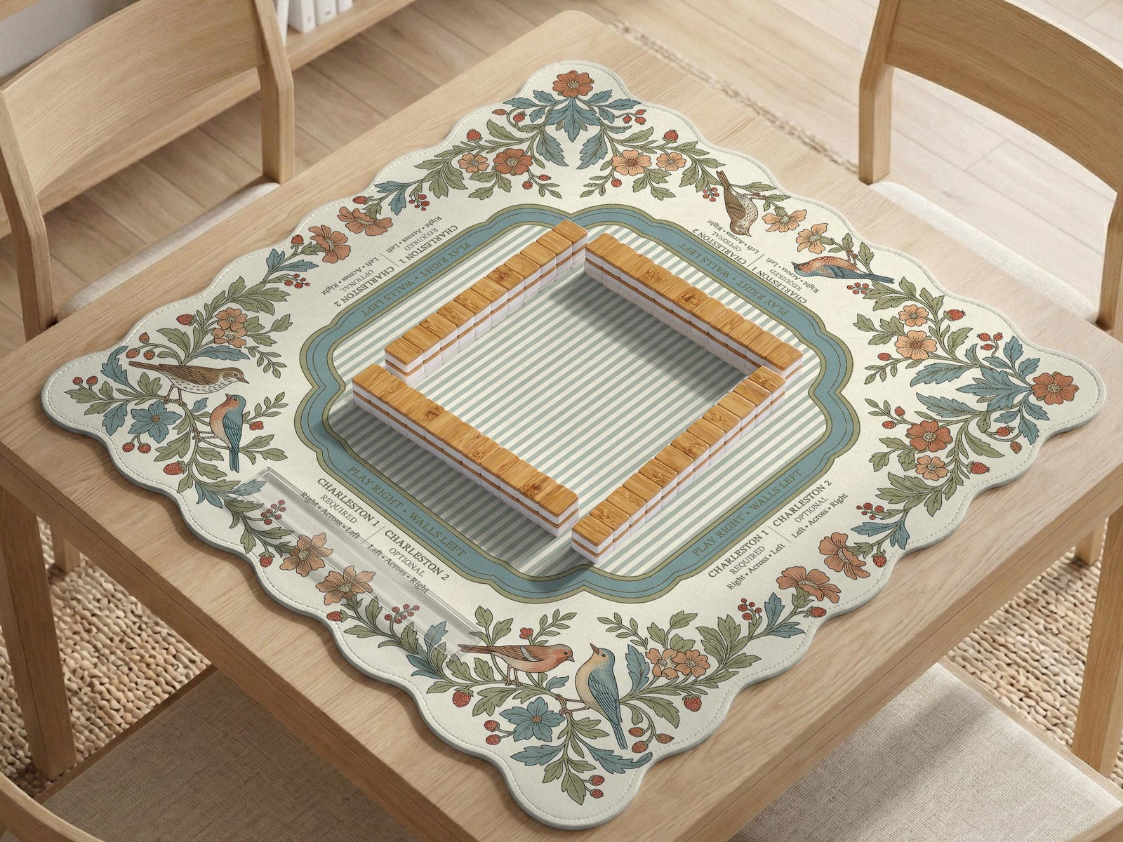 Scalloped square mahjong mat with bird illustrations, cream flowers, sage leaves, and a striped center with printed rules text.