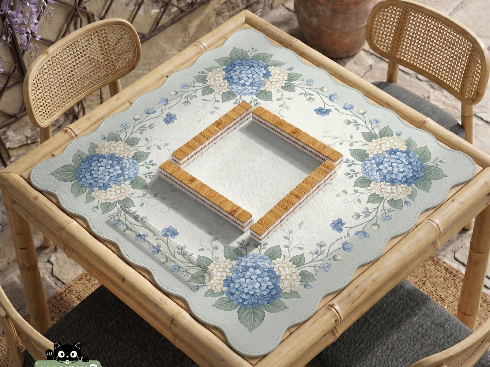 A square blue mahjong mat with hydrangea flowers, cream blossoms, sage leaves, and vines around a plain center play area. The edge is scalloped.