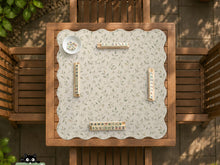 Cream square mahjong mat with a sage vine and leaf botanical pattern and scalloped edges.