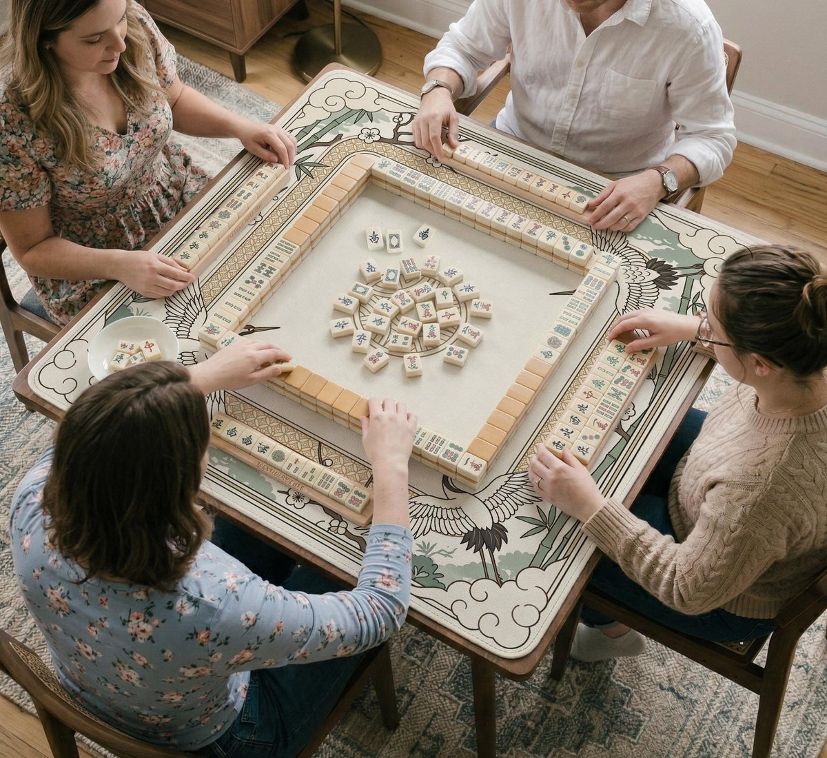 Square mahjong table mat with a cream center and a border design of cranes, bamboo, plum blossoms, and a geometric frame in sage green and warm gold.