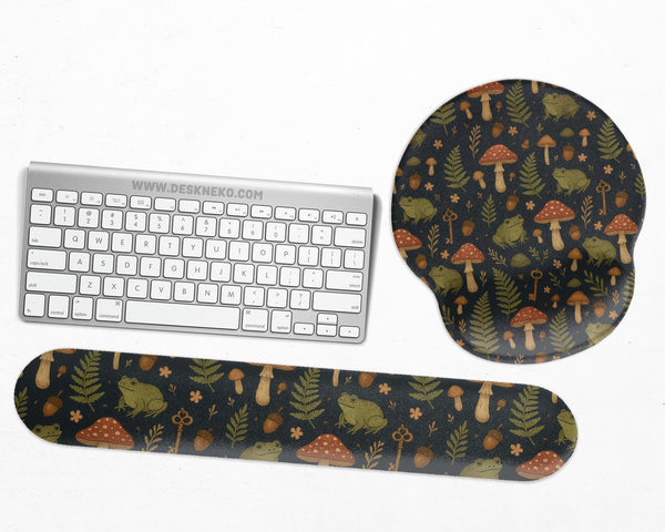 Dark botanical desk mat options with frogs, mushrooms, ferns, and acorns in brown and green tones, plus a matching keyboard wrist rest.