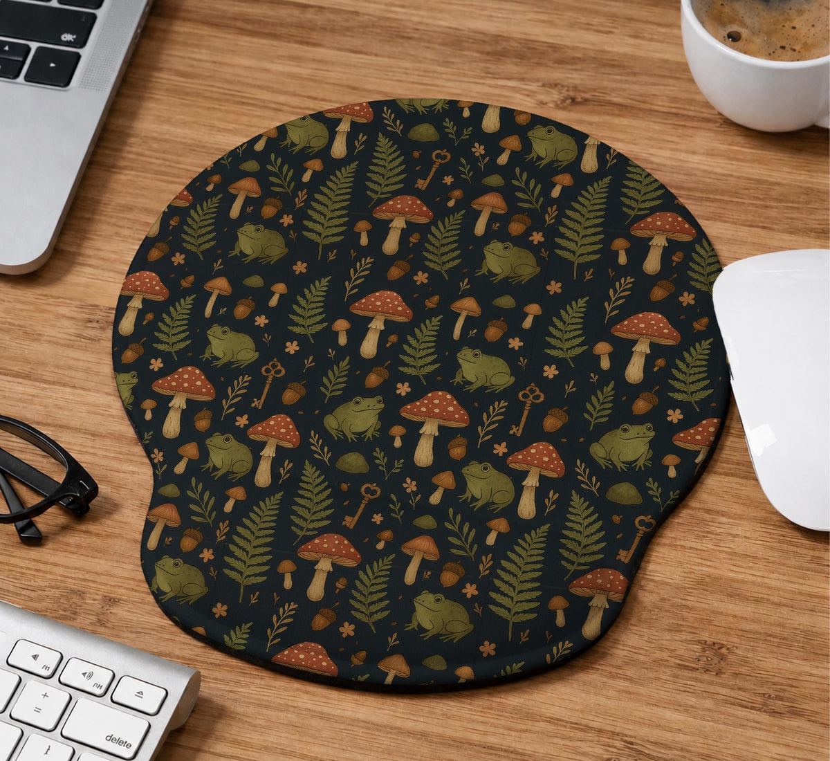 Dark botanical desk mat options with frogs, mushrooms, ferns, and acorns in brown and green tones, plus a matching keyboard wrist rest.