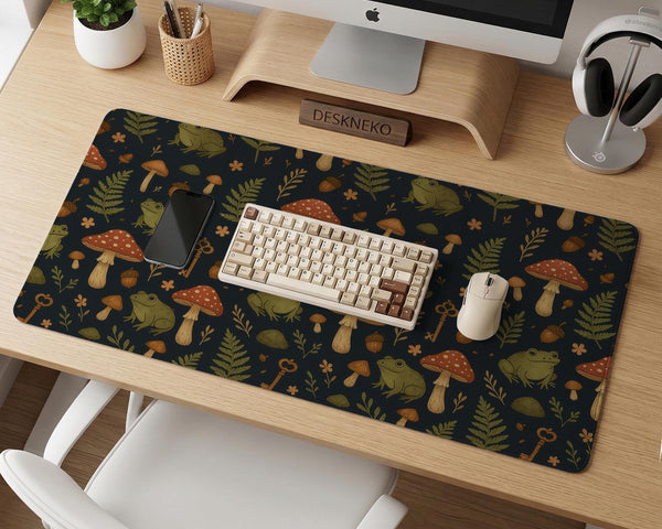 Dark forest-themed desk mat with an all-over pattern of frogs, mushrooms, fern leaves, acorns, tiny flowers, and antique keys.